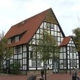 Haus Brinkmann Fachwerkhaus mit roten Ziegeldächern umgeben von Bäumen; ein Mensch steht davor auf dem Platz.