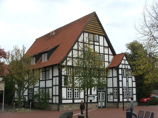Haus Brinkmann Fachwerkhaus mit roten Ziegeldächern umgeben von Bäumen; ein Mensch steht davor auf dem Platz.