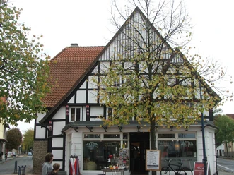 Facherkhaus Lange Straße 103 Fachwerkhaus mit weiß-schwarzem Giebel, Geschäft im Erdgeschoss, herbstlich belaubter Baum davor.