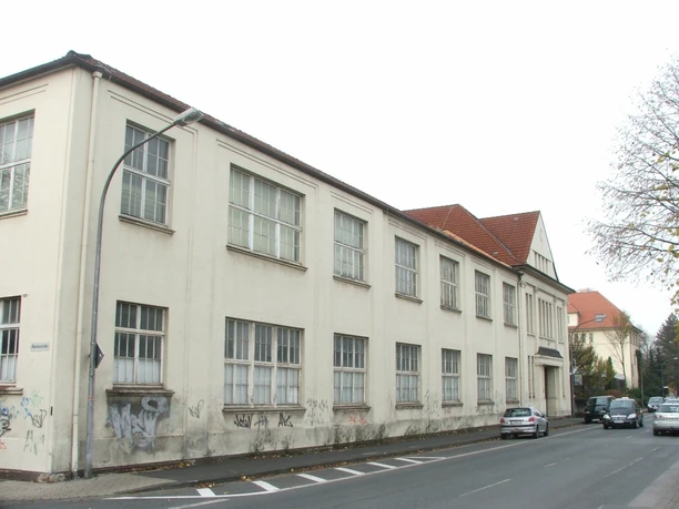 Friedrich-Ebert-Straße 4 Zweistöckiges Gebäude mit altertümlicher Fassade, Graffiti an den Wänden und parkenden Autos davor.