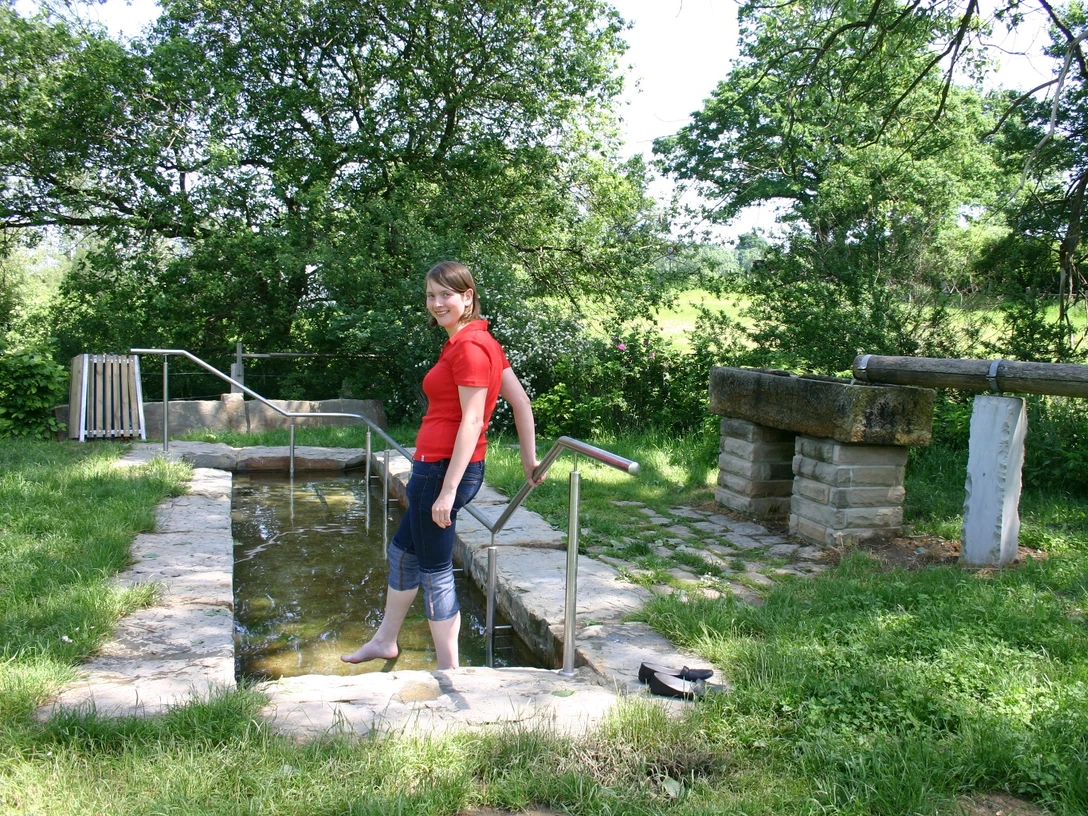 Eine Frau nutzt die Kneipp-Anlage im Golmeketal, umgeben von üppigem Grün und einem klaren Himmel.