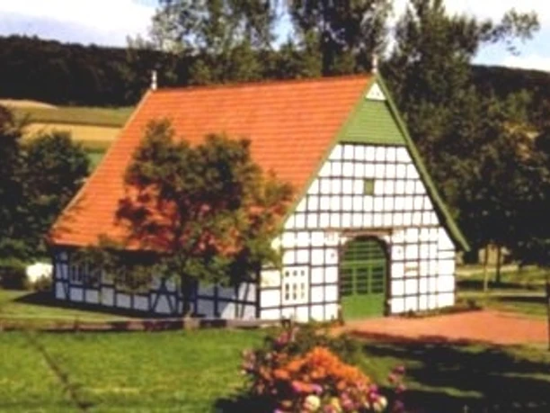 Fachwerkgebäude mit rotem Ziegeldach, umgeben von Wiesen und Bäumen, lädt zur Begegnung ein.