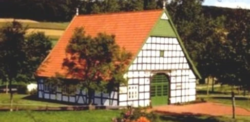 Haus der Begegnung Fachwerkgebäude mit rotem Ziegeldach, umgeben von Wiesen und Bäumen, lädt zur Begegnung ein.