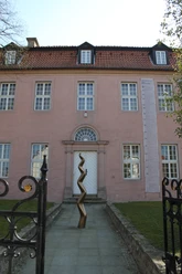 Städtische Galerie Eichenmüllerhaus Ehemaliges Wohnhaus mit rosa Fassade und modernen Kunstskulpturen vor dem Eingang, umgeben von Bäumen.