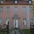 Städtische Galerie Eichenmüllerhaus Ehemaliges Wohnhaus mit rosa Fassade und modernen Kunstskulpturen vor dem Eingang, umgeben von Bäumen.