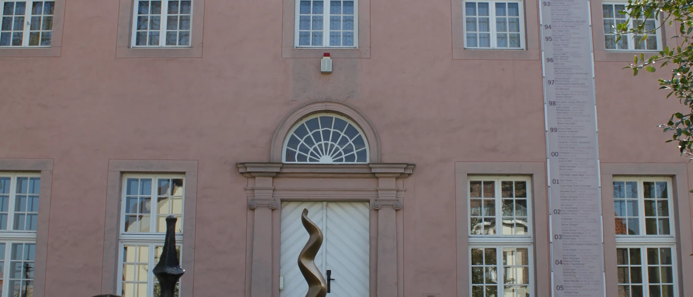 Städtische Galerie Eichenmüllerhaus Ehemaliges Wohnhaus mit rosa Fassade und modernen Kunstskulpturen vor dem Eingang, umgeben von Bäumen.