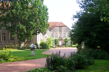 Historisches Kloster Willebadessen mit Ziegelsteingebäude, umgeben von grünen Bäumen und gepflegten Gärten.