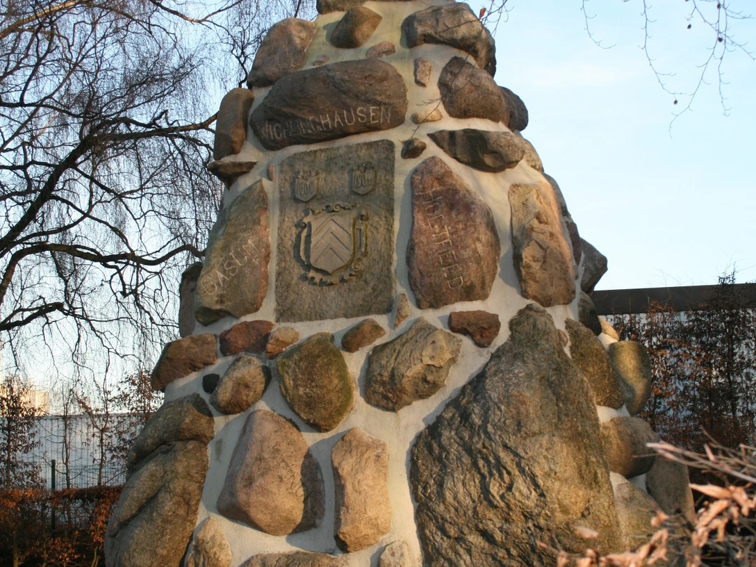 Denkmalfindlingspyramide Ein pyramidenförmiges Denkmal aus großen, unregelmäßigen Feldsteinen, umgeben von kahlen Bäumen.