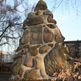 Denkmalfindlingspyramide Ein pyramidenförmiges Denkmal aus großen, unregelmäßigen Feldsteinen, umgeben von kahlen Bäumen.
