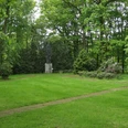 Gedenkpark Grüne Parklandschaft mit einer Skulptur im Hintergrund, umgeben von hohen Bäumen und gepflegtem Rasen.