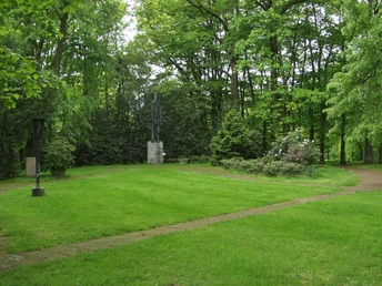 Gedenkpark Grüne Parklandschaft mit einer Skulptur im Hintergrund, umgeben von hohen Bäumen und gepflegtem Rasen.