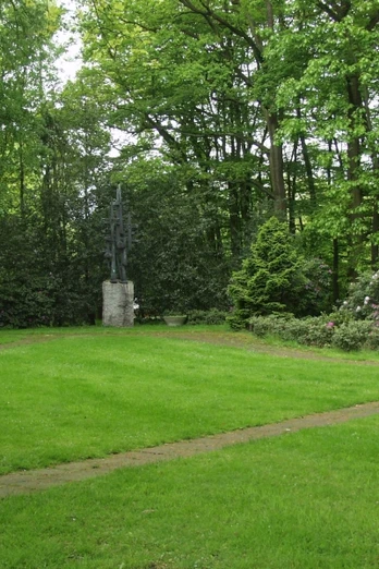 Gedenkpark Grüne Parklandschaft mit einer Skulptur im Hintergrund, umgeben von hohen Bäumen und gepflegtem Rasen.