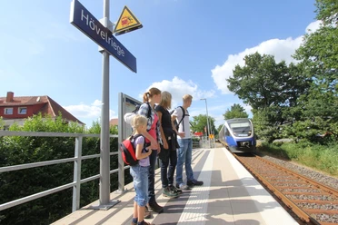 Bahnhof Hövelriege Eine Familie wartet am Bahnhof Hövelriege auf den einfahrenden Zug bei strahlendem Sonnenschein.