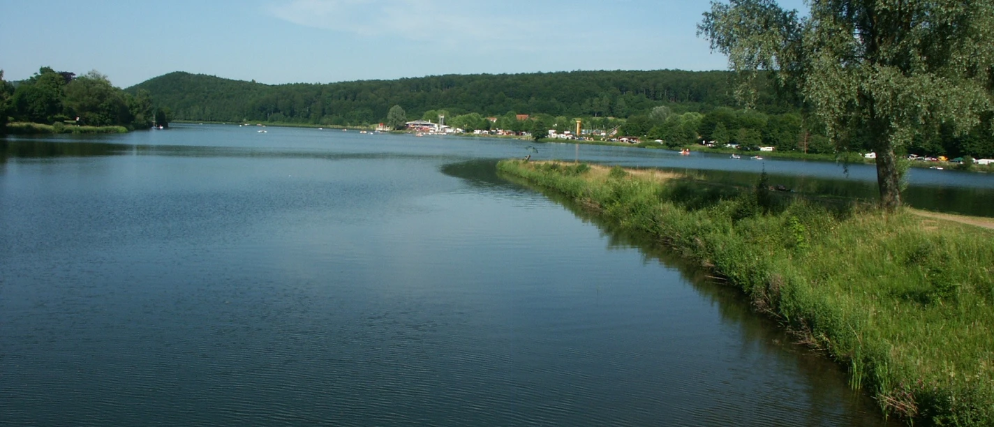 Weitläufiger See mit sanfter Uferlinie, umgeben von Wald und unter blauem Himmel gelegen.