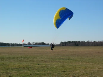 Segelflugplatz Ein Gleitschirmpilot landet auf einem weiten Feld mit blauen und gelben Gleitschirm, klare Sicht.
