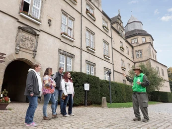 Gruppe von fünf Personen mit einem Führer vor dem historischen Torbogen von Schloss Varenholz.