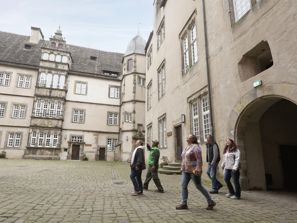 Im Schlossinnenhof Menschen spazieren durch einen historischen Innenhof mit Steinböden, umgeben von alten Gebäuden.