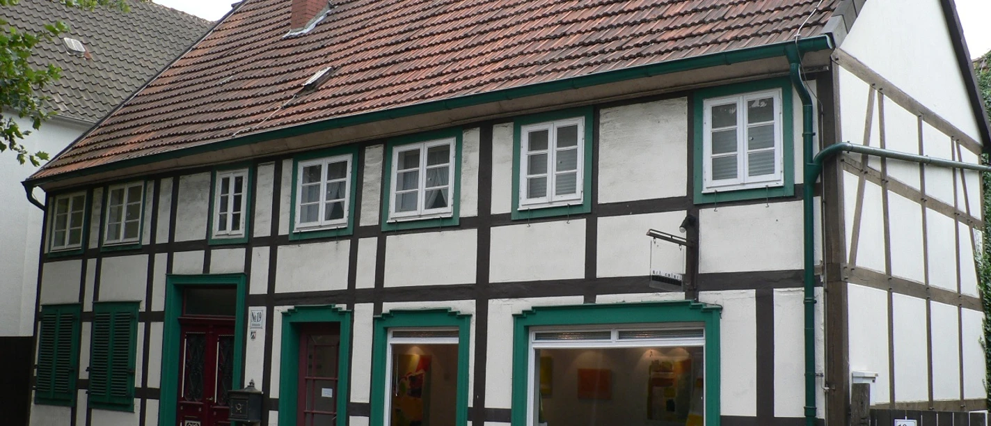 Haus Feldstraße Fachwerkhaus mit roten Ziegeln, grünen Fensterrahmen und zwei Schaufenstern, steht in einer ruhigen Straße.