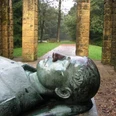 Ehrenmal Gedenkstätte mit liegender Steinskulptur, von Säulen umgeben, in einer bewaldeten Parklandschaft.