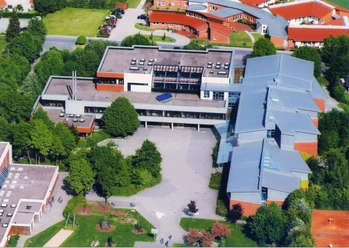 Luftaufnahme eines modernen Gebäudekomplexes mit Flachdächern und angrenzender grüner Landschaft.