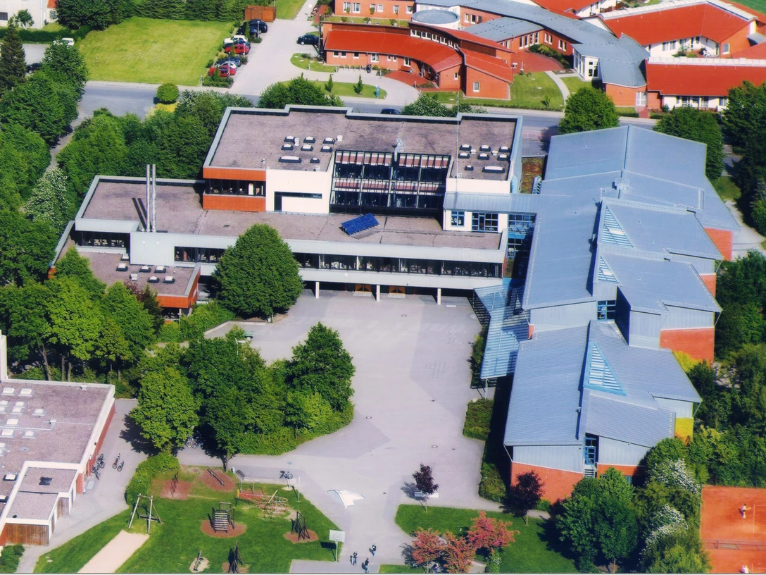 Luftaufnahme eines modernen Gebäudekomplexes mit Flachdächern und angrenzender grüner Landschaft.