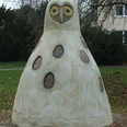 Horst von Hörste Große Beton-Eulenskulptur in einem Park, umgeben von Bäumen und einem Haus im Hintergrund.