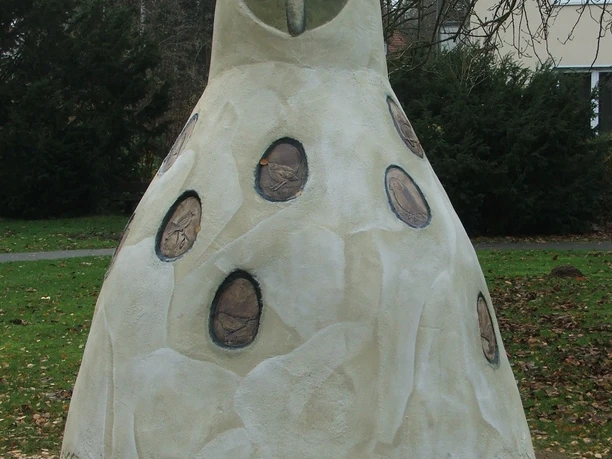Horst von Hörste Große Beton-Eulenskulptur in einem Park, umgeben von Bäumen und einem Haus im Hintergrund.