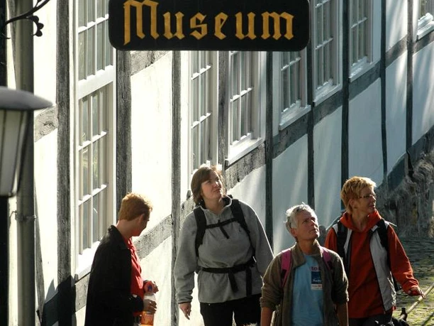 Vier Personen und ein Hund gehen einen gepflasterten Weg entlang, vorbei an einem Fachwerkgebäude mit einem Museumsschild.
