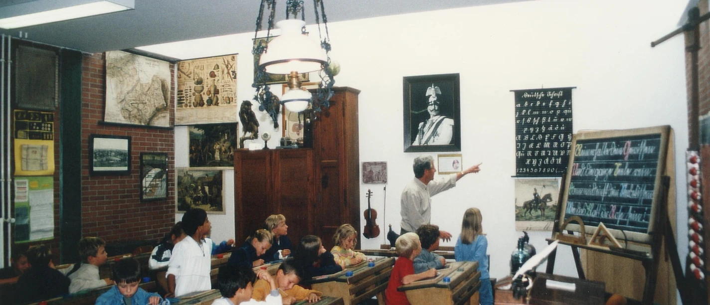 Schulmuseum Büren Ein Lehrer erklärt in einem historischen Klassenzimmer die Schulgeschichte, umgeben von Schautafeln.