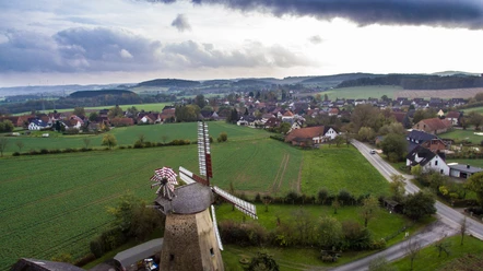 Luftaufnahme einer historischen Mühle umgeben von grünen Feldern und einem ländlichen Dorfpanorama.