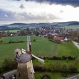 Luftaufnahme einer historischen Mühle umgeben von grünen Feldern und einem ländlichen Dorfpanorama.