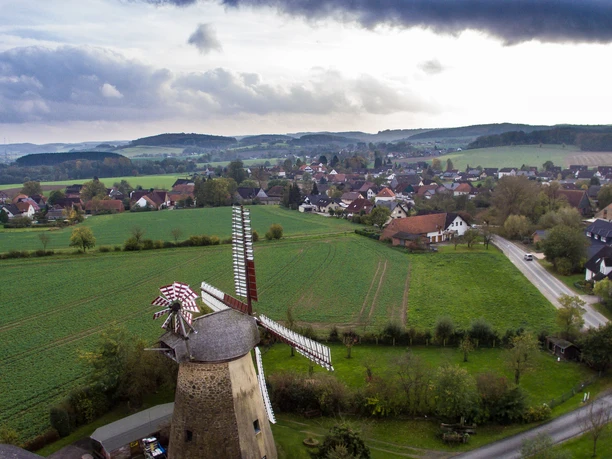 Luftaufnahme einer historischen Mühle umgeben von grünen Feldern und einem ländlichen Dorfpanorama.