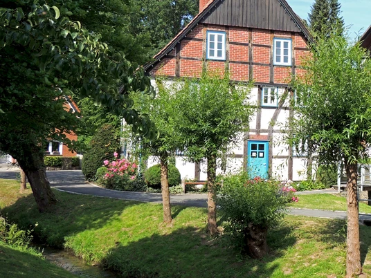 Corves Mühle an der Kalle Altes Fachwerkhaus mit rotem Ziegeldach, flankiert von Bäumen, inmitten gepflegter Grünanlage.