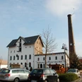 Ehemalige Kornbrennerei Meyer & WEZ Historische Backsteinbrennerei mit Schornstein, vor modernem Eingang platziert, flankiert von Autos.