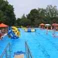 Ein lebhaftes Schwimmbad voller Menschen mit aufblasbaren Spielgeräten und grünen Bäumen im Hintergrund.