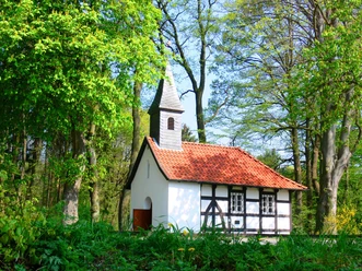 Brinkkapelle Weiße Kapelle mit rotem Ziegeldach, umgeben von grünen Bäumen und einem sonnigen Himmel.