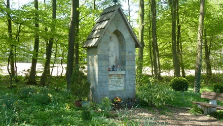 Steinernes Wegekreuz umgeben von blühendem Frühlingslaub im schattigen Waldbereich bei Borchen-Dörenhagen.