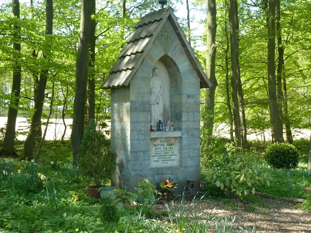 Steinernes Wegekreuz umgeben von blühendem Frühlingslaub im schattigen Waldbereich bei Borchen-Dörenhagen.