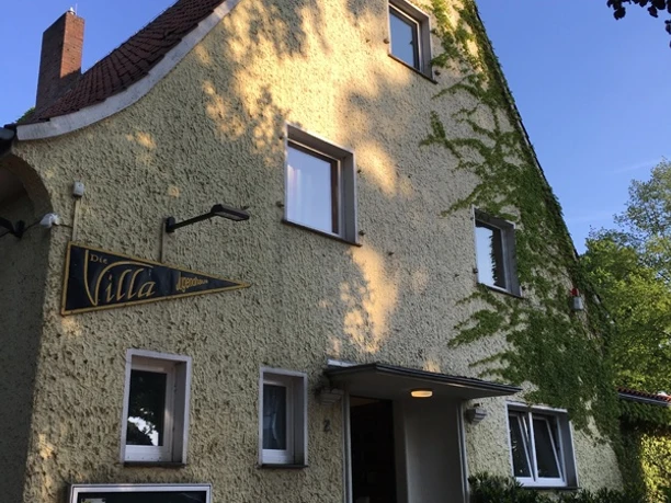 Gelbes, mit Efeu bewachsenes Gebäude unter blauem Himmel. Fahrräder parken vor dem Eingang.