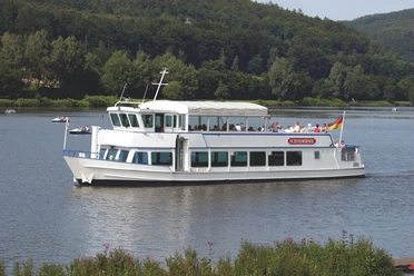 SchiederSee mit Schifffahrt Weißes Ausflugsschiff mit Passagieren gleitet auf einem See, umgeben von grünen Wäldern und sanften Hügeln.