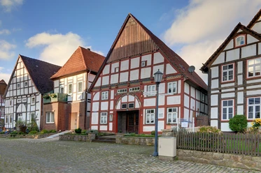 Zwei historische Fachwerkhäuser stehen nebeneinander; rotes Ziegeldach, strahlend weiße Fassade.