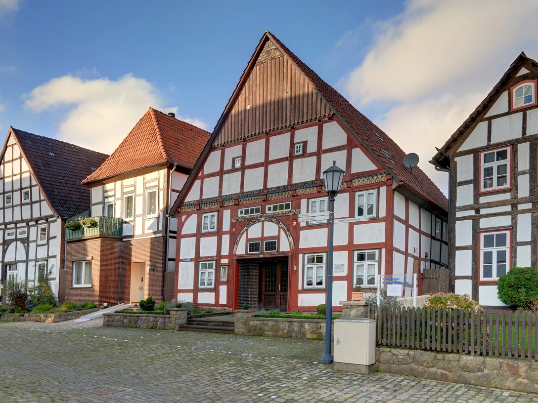 Zwei historische Fachwerkhäuser stehen nebeneinander; rotes Ziegeldach, strahlend weiße Fassade.