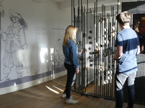 Zwei Personen betrachten interaktive Inhalte in einem historischen Ausstellungsraum mit Wandgestaltung.