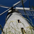 Historische Windmühle Bavenhausen mit hölzernen Flügeln, aus niedriger Perspektive vor blauem Himmel.