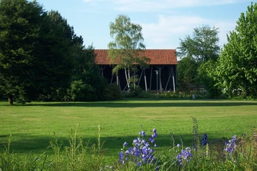 Salinenpark Grüner Park mit Blüten und Gradierwerk, umgeben von Bäumen und einem roten Ziegeldach.