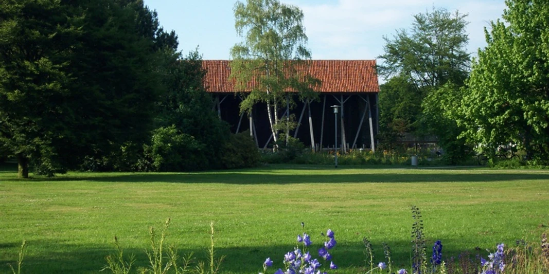 Salinenpark Grüner Park mit Blüten und Gradierwerk, umgeben von Bäumen und einem roten Ziegeldach.