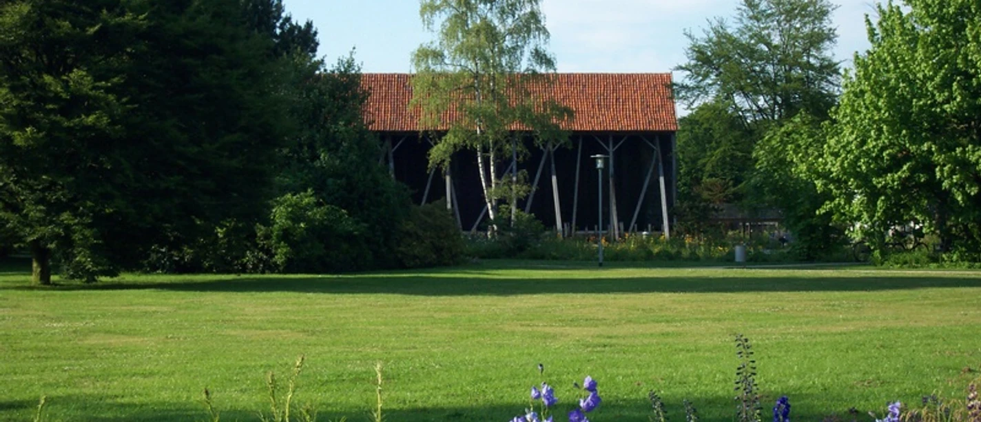 Salinenpark Grüner Park mit Blüten und Gradierwerk, umgeben von Bäumen und einem roten Ziegeldach.