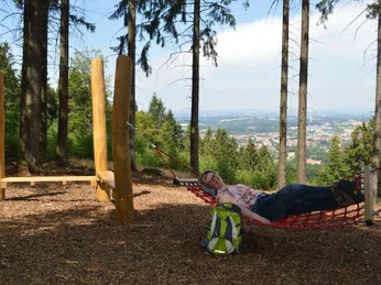 Hörstation Werther Frau entspannt in Hängematte, umgeben von Bäumen, mit Blick auf eine weite Landschaft im Hintergrund.