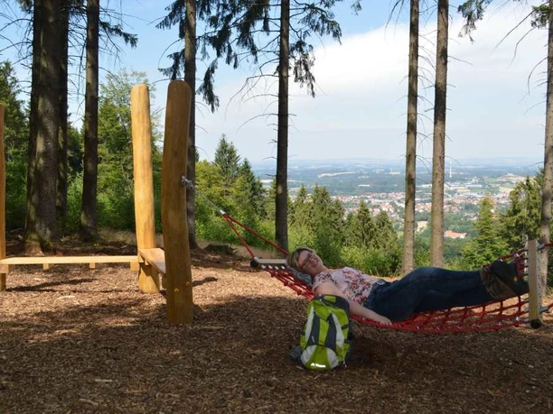 Hörstation Werther Frau entspannt in Hängematte, umgeben von Bäumen, mit Blick auf eine weite Landschaft im Hintergrund.