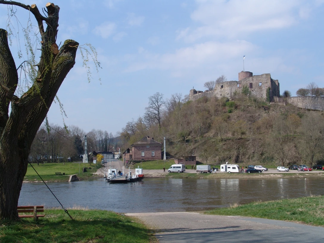 Blick auf die historische Burg Polle mit der Weser im Vordergrund, eine Fähre kreuzt den Fluss.